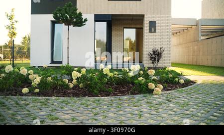 Façade de maison moderne avec jardin bien entretenu, présentant des hortensias en fleurs et un revêtement perméable dans la cour avant Banque D'Images