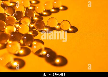 Des billes en verre sont disposées sur une surface jaune vif, mettant en valeur les reflets et les ombres qui accentuent leur qualité transparente et leur attrait visuel Banque D'Images