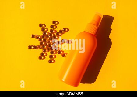 Bouteille pulvérisatrice jaune avec pompe placée à côté d'un amas en forme d'étoile de capsules dorées sur une surface jaune vif Banque D'Images