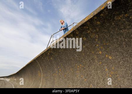 Jeune femme solitaire debout au sommet du mur de défense contre les vagues contemplant l'horizon Banque D'Images