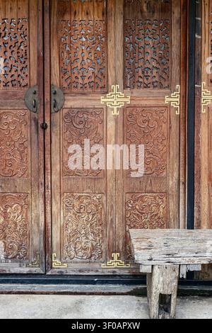 Porte en bois sculpté rustique avec des motifs floraux complexes et un banc vintage sur un sol en pierre offrant un fond architectural authentique. Banque D'Images