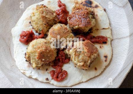 Vue aérienne de cinq boules de falafel dorées avec sauce tomate sur une galette grillée dans un bol en bois rustique, lumière naturelle douce Banque D'Images