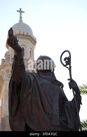 Cliché architectural et artistique capturant une statue en bronze ou en métal sombre d'un saint ou d'un évêque tenant un bâton pastoral et levant une main en bénédiction, Banque D'Images