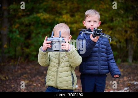 Enfants utilisant un drone dans le parc d'automne, un garçon tenant quadcopter et un autre le contrôlant avec télécommande, technologie extérieure et concept d'apprentissage Banque D'Images