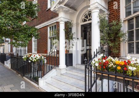 Façade élégante d'une maison de ville londonienne avec des colonnes blanches et des jardinières fleuries Banque D'Images