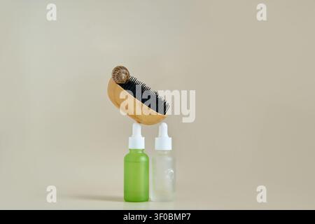 Brosse en bois avec escargot posé sur des flacons goutteurs verts et givrés sur une table beige neutre dans une composition minimaliste en studio. Banque D'Images