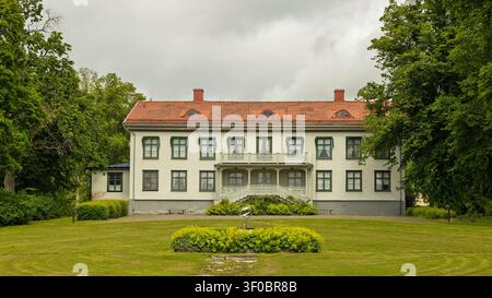 Karlskoga, Suède - 18.06.2026 : un grand domaine de deux étages avec une façade blanche, un toit en terre cuite et un balcon orné au milieu d'un jardin bien entretenu Banque D'Images