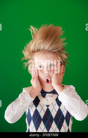 Enfant surpris en classe. Enfant drôle devant un fond de tableau vert. Concept de retour à l'école et d'éducation Banque D'Images
