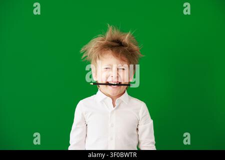 Enfant heureux en classe. Enfant drôle devant un fond de tableau vert. Concept de retour à l'école et d'éducation Banque D'Images