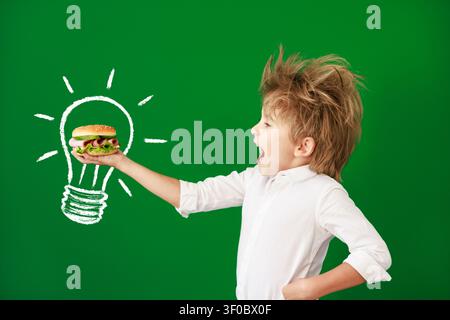 Enfant surpris en classe. Enfant drôle devant un fond de tableau vert. Concept de retour à l'école et d'éducation Banque D'Images