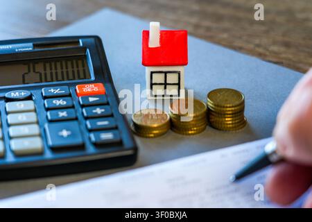 Calculateur, maison miniature et pièces empilées représentent la planification hypothécaire, le financement immobilier, la budgétisation, l'épargne et l'investissement immobilier Banque D'Images