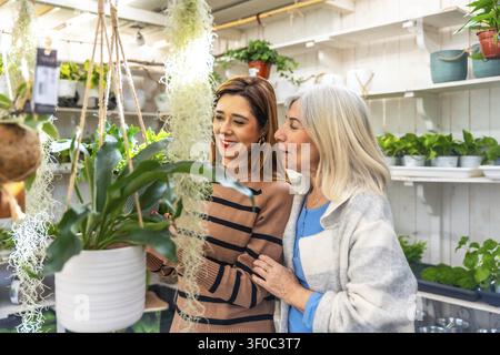 Mère âgée et fille adulte souriant en choisissant des plantes d'intérieur en pot dans un jardin lumineux, profitant d'un moment de qualité et de leur amour partagé pour le vert Banque D'Images