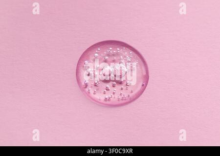 Grossissement d'une bulle de sérum rose sur du papier texturé pour un concept de beauté et de soins de la peau Banque D'Images