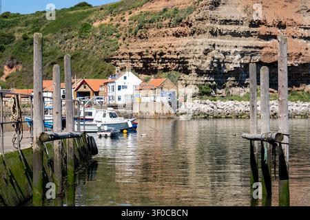Focus sélectif sur la jetée en béton et les poteaux d'amarrage en bois du port de Staithes, avec un arrière-plan légèrement flou mettant en valeur la texture et la côte Banque D'Images
