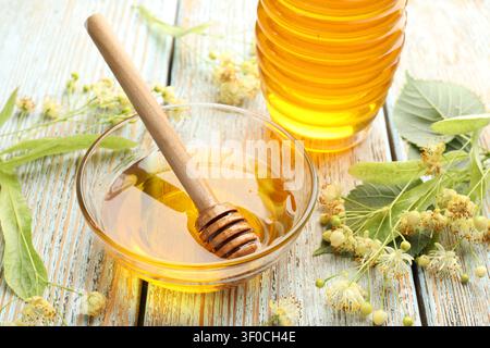 Miel de tilleul naturel dans un bol avec trempette, pot et fleurs sur une vieille table en bois, gros plan Banque D'Images