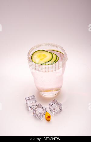une poupée en caoutchouc et des glaçons devant un verre de gin-tonic avec un bord sucré et des tranches de concombre. Banque D'Images