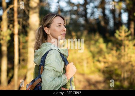 Femme positive et confiante en randonnée dans la forêt avec un sac à dos, debout regardant le soleil et profitant d'un repos tranquille Banque D'Images
