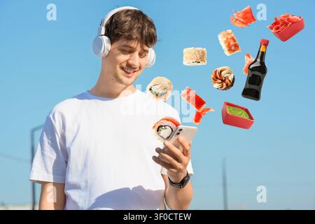 Jeune homme utilisant un smartphone avec des sushis flottants et des condiments Banque D'Images