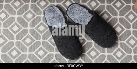 Paire de chaussons noirs flous sur tapis à motifs Banque D'Images