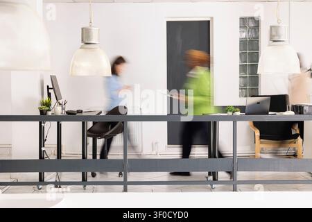 Un bureau moderne animé montre des employés divers marchant dans une flou de mouvement, créant un sentiment d'activité d'entreprise rapide. Des professionnels multiethniques se déplacent sur le lieu de travail, travaillant vers les délais du bureau. Banque D'Images