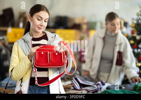 Positive jeune femme choisissant sac à main dans le magasin de vêtements Banque D'Images