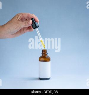 Main féminine tenant une pipette en verre avec de l'huile qui coule sur une bouteille d'huile essentielle. Concept de beauté ou de santé. Banque D'Images