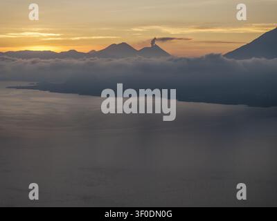 Vue aérienne du lac Atitlán au lever du soleil avec des pics volcaniques et des nuages sur l'eau dans le département de Sololá, Guatemala. Banque D'Images