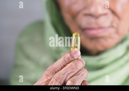 Ancienne femme tenant avec soin une petite capsule d'huile de poisson Banque D'Images