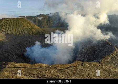Vue aérienne du cratère du mont Bromo avec une épaisse fumée volcanique s'élevant de la caldeira accidentée et des gens marchant le long du bord à Tosari, Java oriental, Indo Banque D'Images