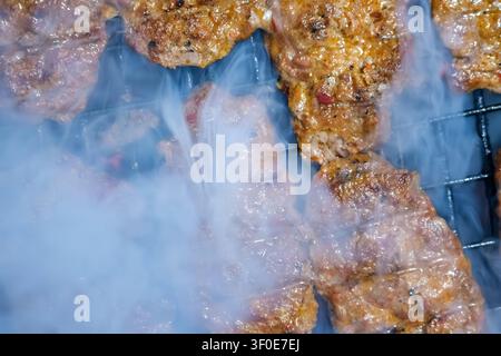 Vue rapprochée de steaks ou de galettes de viande hachée bien assaisonnés cuisant lentement sur une grille de barbecue grésillant, produisant une fumée épaisse et appétissante Banque D'Images