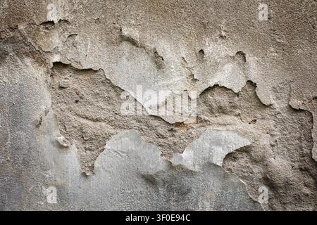 Texture d'une structure en béton endommagée. Vue détaillée du plâtre ébréché, de la vieille surface grise et du revêtement en ciment fissuré sur un mur en béton industriel. Banque D'Images