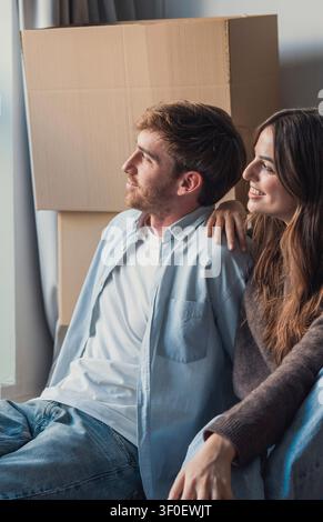 Jeune couple se détend et sourit dans leur nouvel appartement entouré de cartons d'emménagement, profitant d'un moment calme ensemble après avoir déballé et installé Banque D'Images