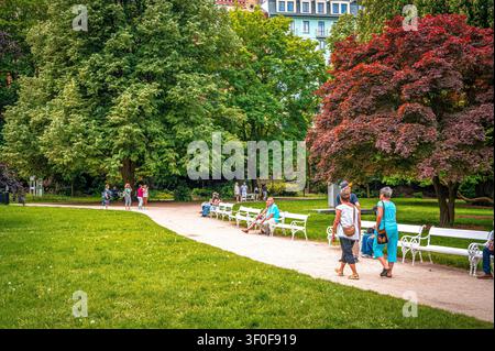 Les gens se promènent dans le parc de la ville de Karlovy Vary. Certains sont assis sur des bancs et profitent de la nature. Des arbres se dressent le long du chemin. C'est une belle journée à th Banque D'Images