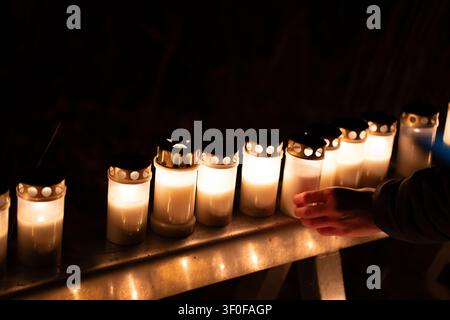 Person tenant une bougie commémorative allumée à l'extérieur la nuit avec des bougies brillantes en arrière-plan, Jour des Morts au cimetière de Skogskyrkogarden à Stockholm, Suède Banque D'Images
