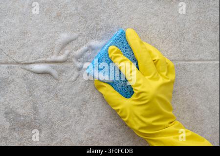 gros plan d'une personne essuyant un mur de salle de bain avec une éponge bleue Banque D'Images
