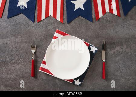 Assiette blanche, serviette patriotique, couverts rouges et fanions festifs sur fond gris avec espace libre. Vue de dessus. Banque D'Images