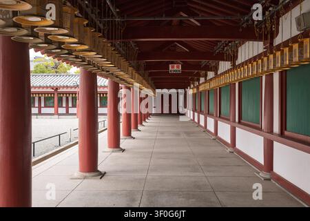 Vue architecturale en perspective d'un long couloir en bois couvert et vide avec des lanternes dorées ornées au temple Shitenno-ji, Osaka, Japon Banque D'Images