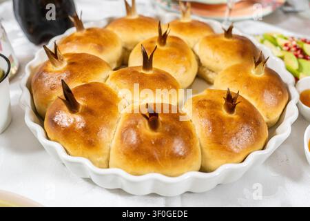 Des rouleaux de challah en forme de grenade dorée reposent sur une assiette à motifs, prêts pour une douce célébration juive du Nouvel An à Rosh Hashanah à la maison. Banque D'Images