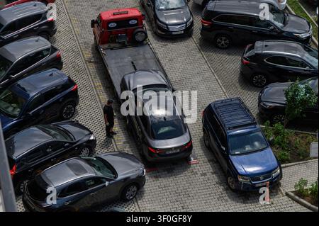 8 juillet 2026, Tbilissi, Géorgie Une photographie aérienne en hauteur montrant un camion de remorquage rouge chargeant activement une berline grise dans un parking pavé bondé. Banque D'Images