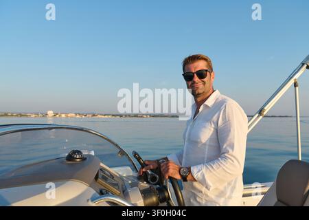 Homme conduisant un bateau près de la côte avec des lunettes de soleil pendant une soirée d'été calme style de vie de capitaine de yacht Banque D'Images