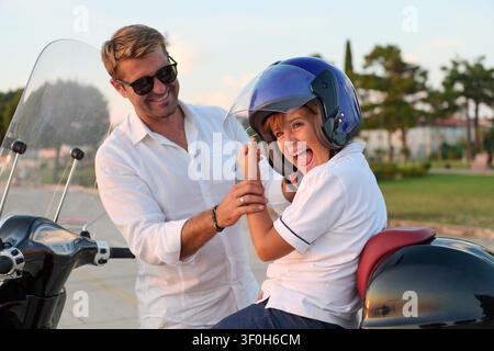 Père aidant son fils à mettre son casque tout en roulant ensemble en scooter pendant les vacances d'été amusement en famille Banque D'Images