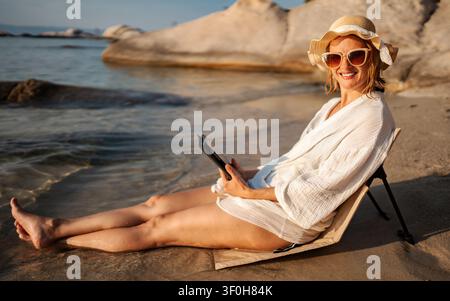 Femme se relaxant sur la plage en lisant sur une tablette numérique Banque D'Images