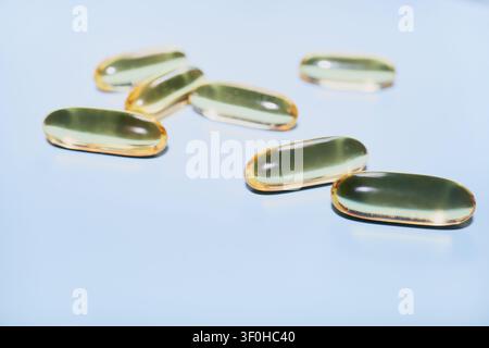 Gélules d'huile de poisson dispersées sur un fond bleu clair, représentant le bien-être et la nutrition Banque D'Images