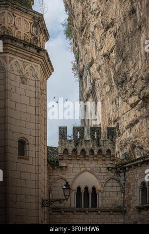 Vue de l'architecture historique en pierre de Rocamadour nichée contre une imposante falaise calcaire sous un ciel nuageux à Rocamadour, Occitanie, Fra Banque D'Images