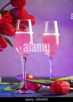 Deux verres de champagne ou de vin rose et un bouquet de tulipes rouges. lumière néon Banque D'Images