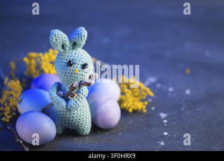 Œufs peints de Pâques, lapin de Pâques avec branche de saule sur une table bleue en béton et espace de copie Banque D'Images