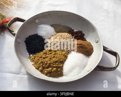 Plan élevé de cumin, cannelle, sucre et graines de sésame dans une poêle rustique, mettant en valeur les ingrédients traditionnels utilisés dans la pâtisserie crétoise et la cuisine grecque. Banque D'Images