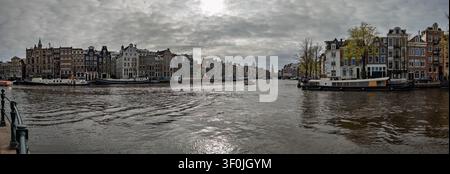 AMSTERDAM, PAYS-BAS - 1ER AVRIL 2026 : Vue panoramique des maisons classiques du canal et des péniches traditionnelles le long de l’Amstel Banque D'Images