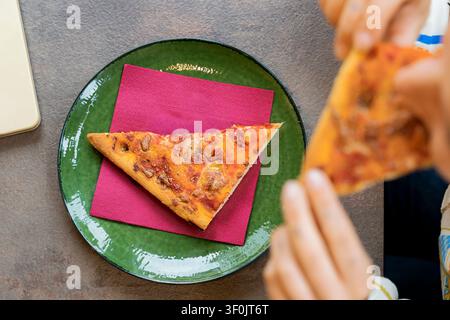 Une personne savourant une part de pizza pendant une pause déjeuner, prenant un moment pour se détendre après une journée de travail bien remplie et profiter d'un équilibre entre travail et loisirs. Banque D'Images