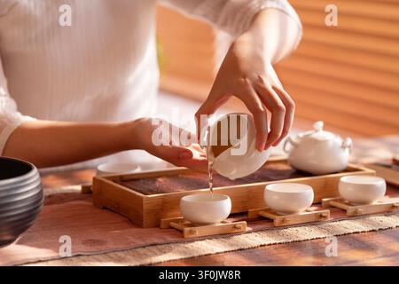 Des mains versant du thé chaud d'une carafe en céramique blanche dans une petite tasse lors d'une cérémonie du thé traditionnelle. Banque D'Images